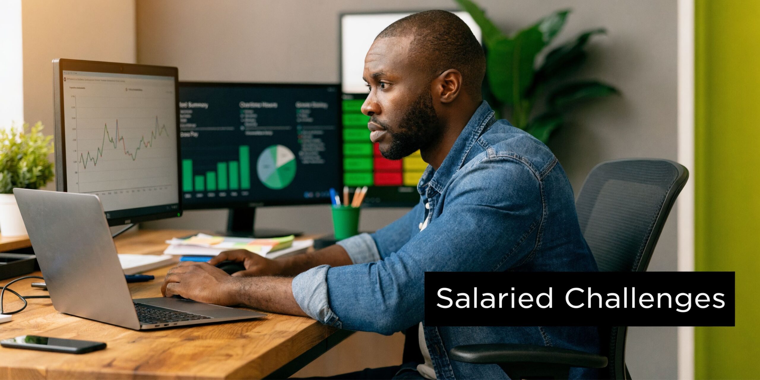 A professional man working on a laptop at a desk with multiple monitors displaying data charts.
